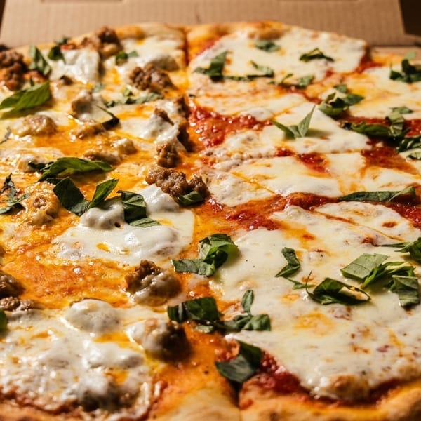 Half sausage and half Margherita pizza with fresh basil in a cardboard box.