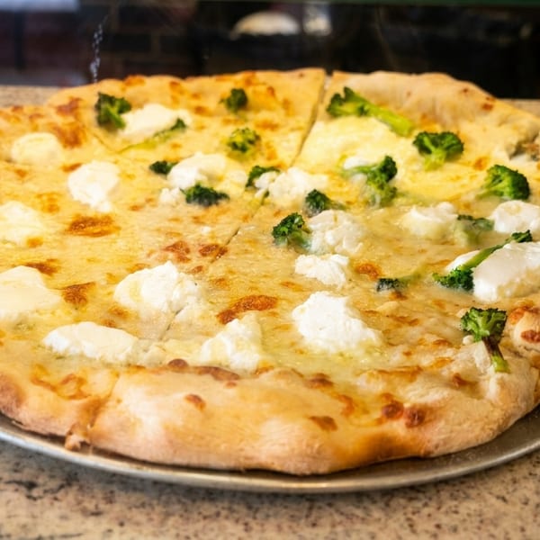 A whole pizza with white cheese and dollops of ricotta, half topped with broccoli florets.
