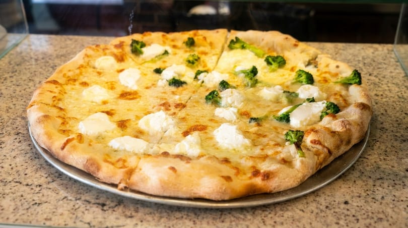 A whole pizza with white cheese and dollops of ricotta, half topped with broccoli florets.
