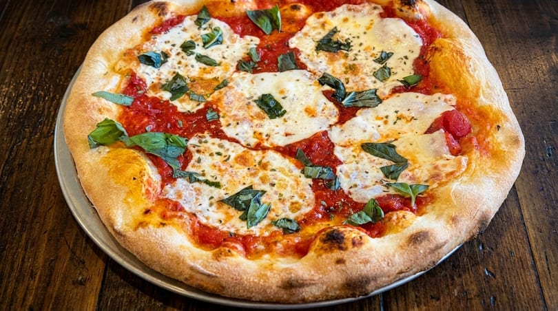 A freshly baked Margherita pizza with melted mozzarella, red sauce, and basil on a wooden table.